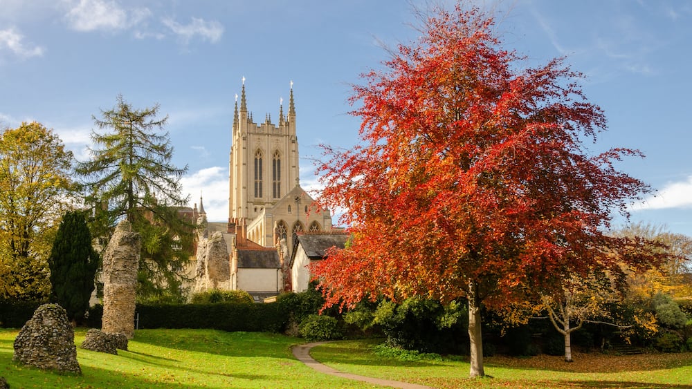 A church with a tall spire, surrounded by autumn-colored trees and a stone wall.