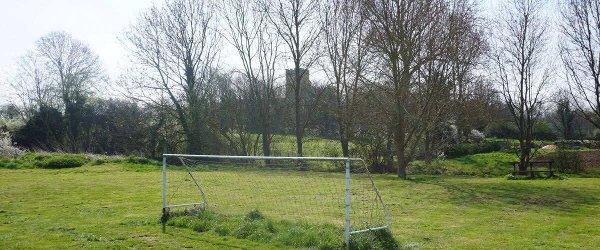 A soccer goal in a grassy field with trees and a stone structure in the background.