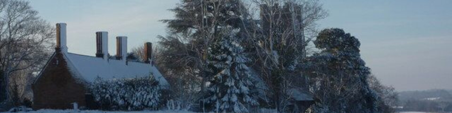 View southwest across a snowy field at Elmswell, Suffolk. On the left are the almshouses, built in 1614. Centre right behind the trees is the parish church of St John the Divine