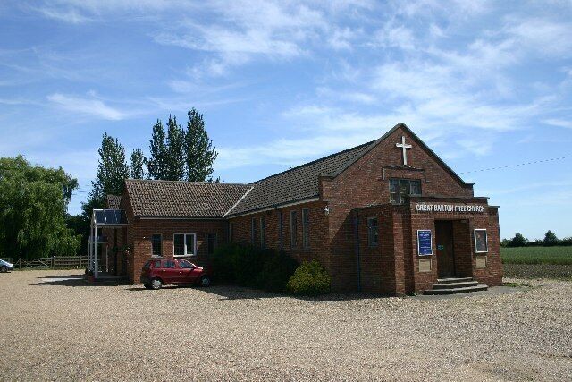 A brick church with a cross on the roof, a red car parked in front, and a sign that reads "Great Haywood Free Church".