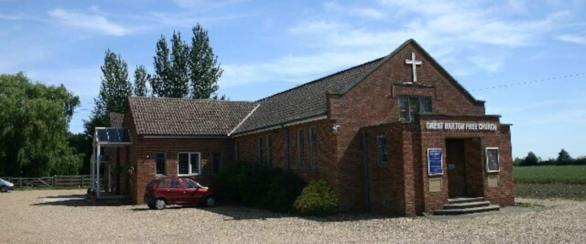 A brick church with a cross on the roof, a red car parked in front, and a sign that reads "Great Haywood Free Church".