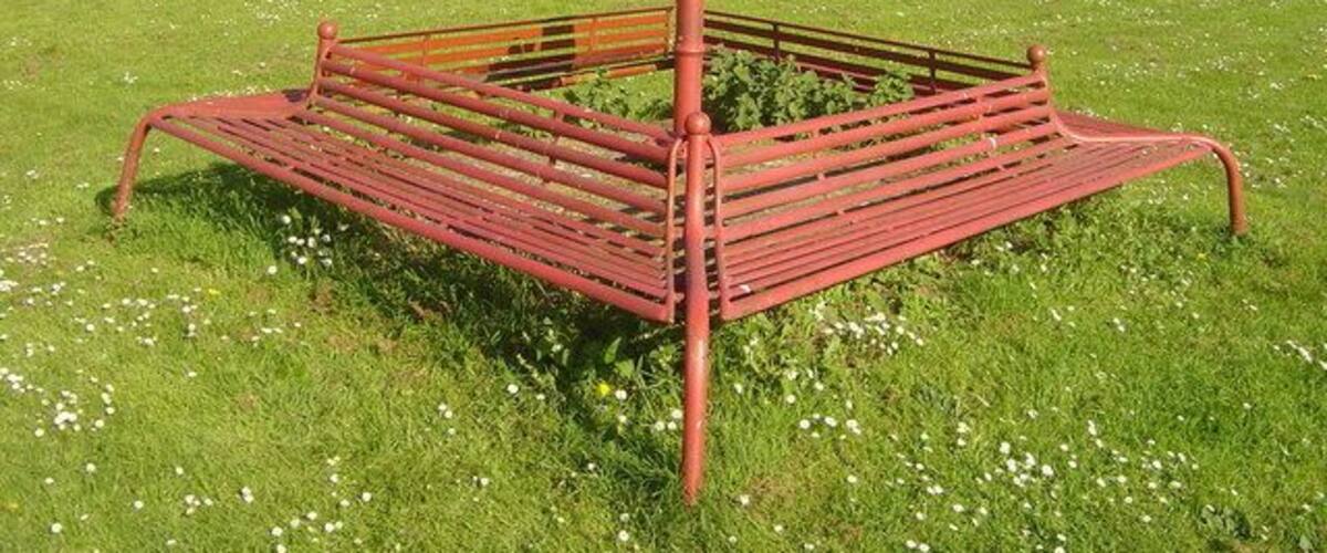 A red metal bench in a grassy field with a soccer goal in the background.