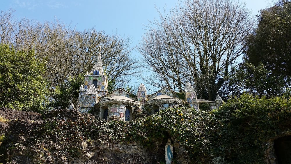 Une église dont le sol est recouvert de mosaïques, avec un clocher entouré d’arbres et de verdure.