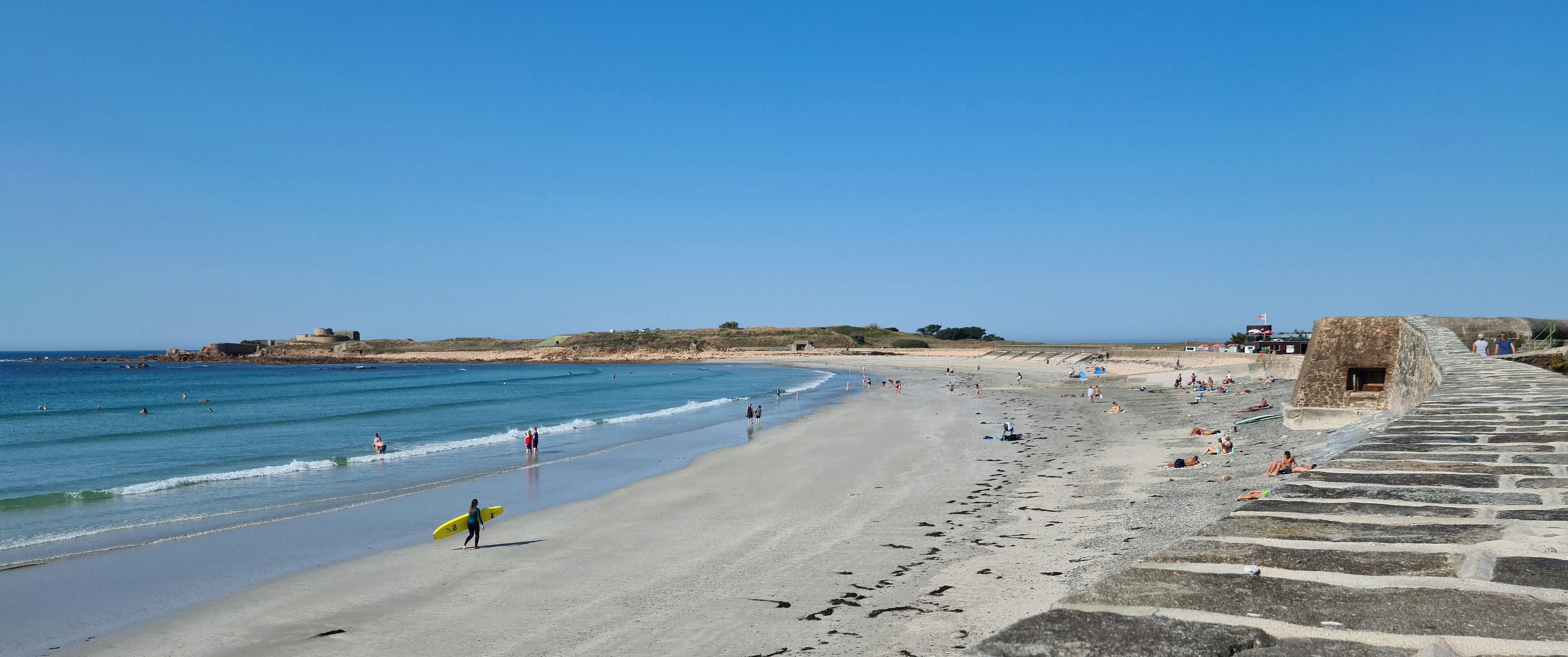 A beach with a stone wall and a clear blue sky.