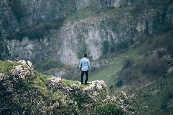 Une personne se tient debout sur un promontoire rocheux, d’où elle domine un paysage montagneux.