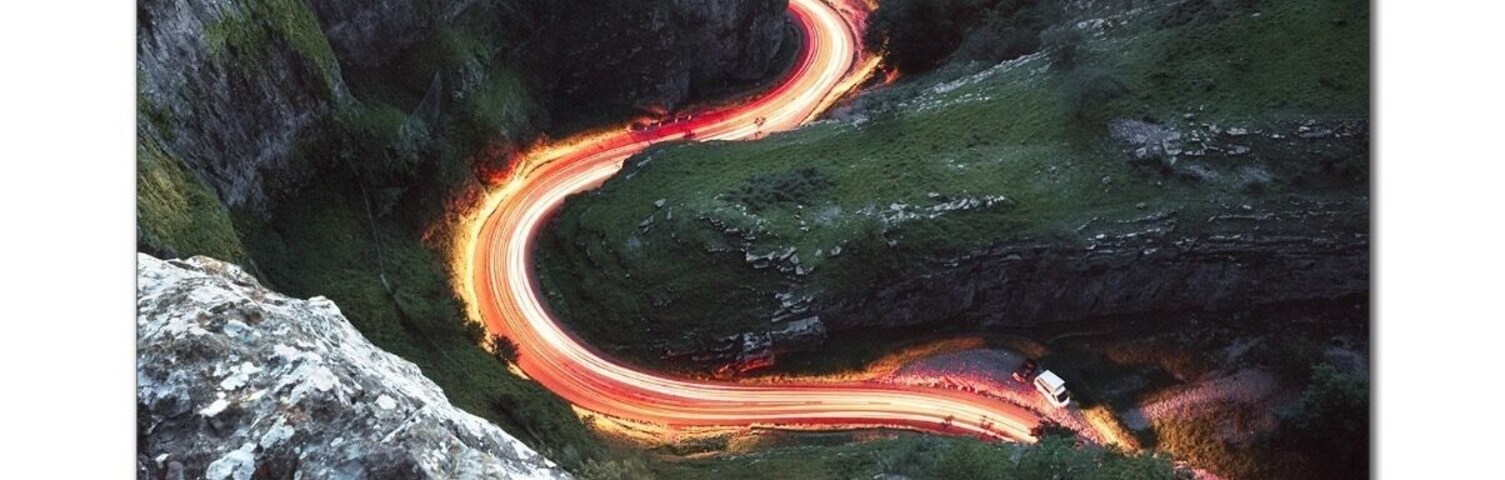 Una carretera sinuosa atraviesa un desfiladero montañoso con afloramientos rocosos y vegetación.