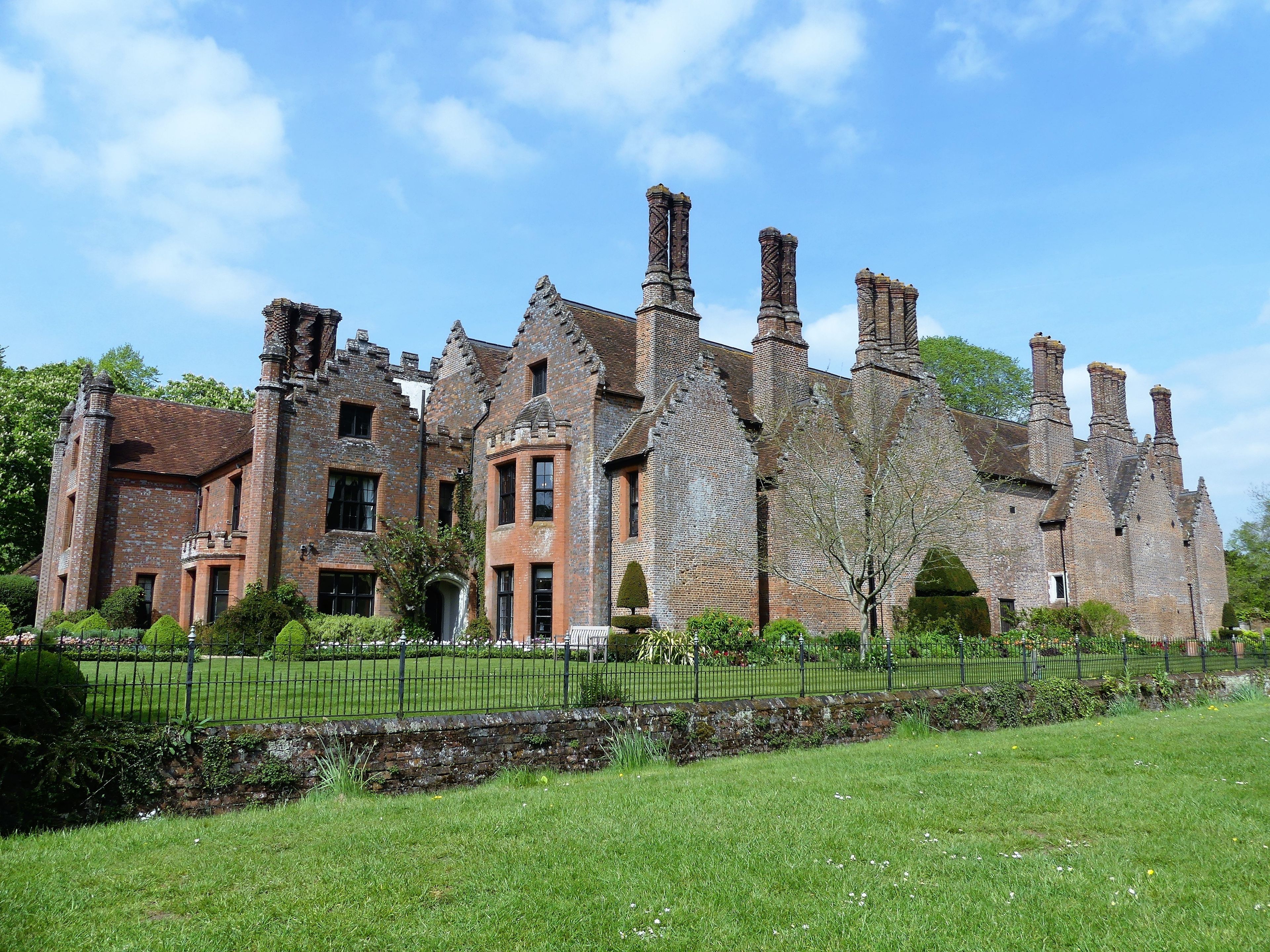 A historic brick building with multiple chimneys and a well-maintained garden.