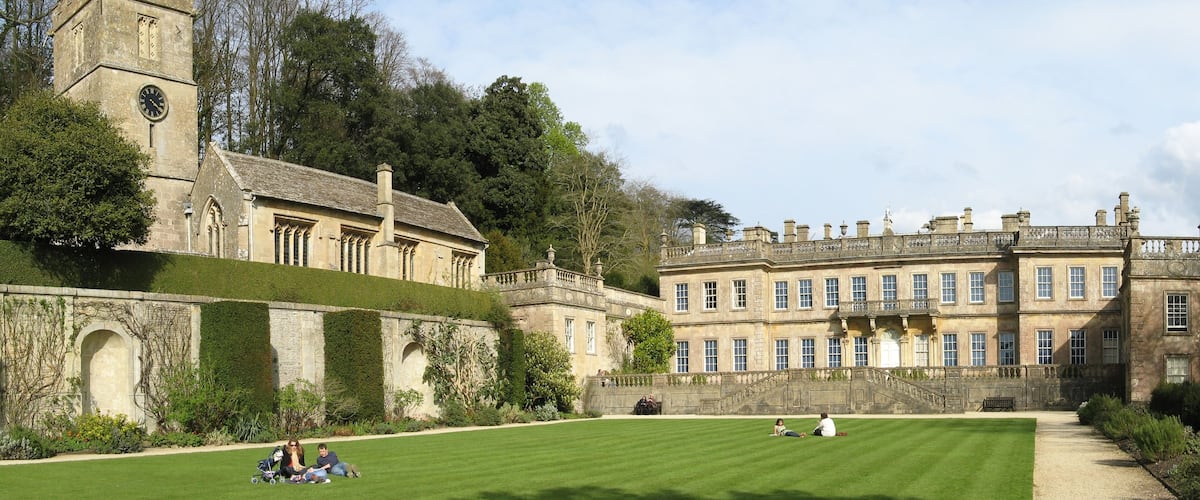 A historic building with a clock tower and a large lawn with people relaxing.