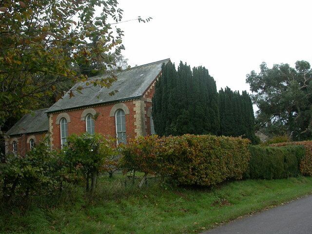 Methodist Chapel, Chittoe Heath A simple rectangular chapel with rear extension, built of red brick with yellow detail. The front is partially obscured by yew trees. A label on the front proclaims "Primitive Methodist 1882".