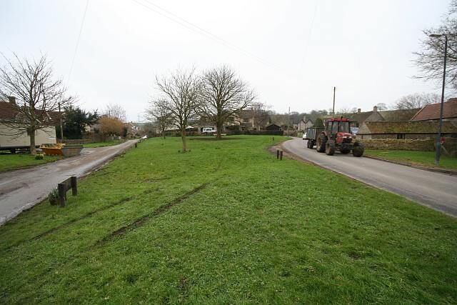 A rural road with a tractor on the right and houses on the left.