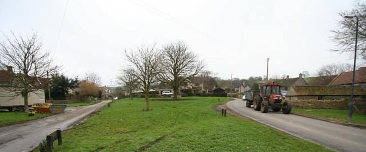 A rural road with a tractor on the right and houses on the left.