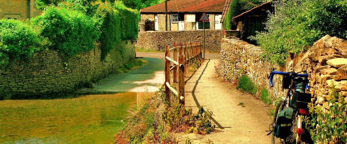 A narrow path beside a river, a stone wall, and a bicycle.