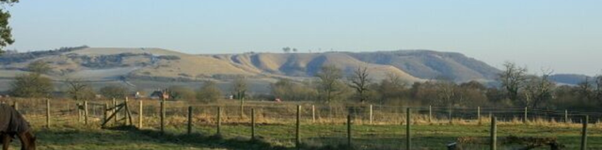 East from the A3102 near Bromham. At the start of a footpath between the A3102 and Bromham. Traffic on the A342 can be seen. The range of hills in the distance, on the edge of the Marlborough Downs, reading from right to left are Roundway, then Oliver's Castle SU0064 with a few trees on top, and Beacon Hill. Between the last two there an unusual bit of corrugated hillside, an explanation for which can be found in 870366 1115212 gives a similar view of these hills from a different direction.