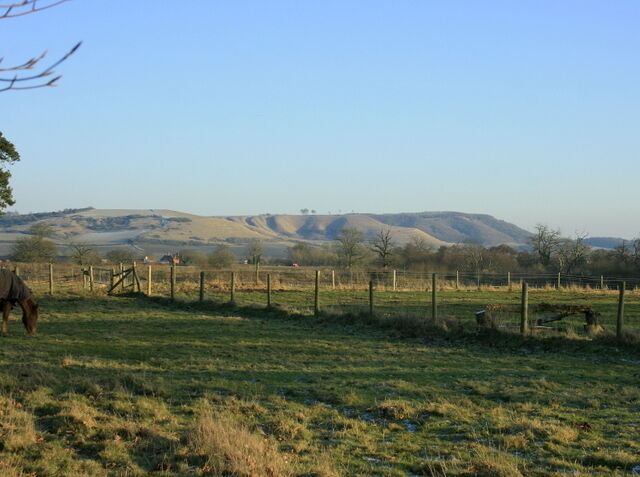 A horse grazing in a fenced field with rolling hills in the background.