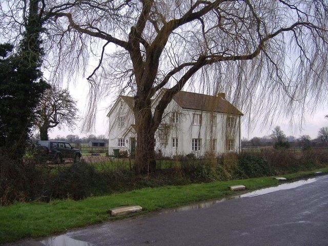 A large white house with a tree in front, a road, and a car parked nearby.