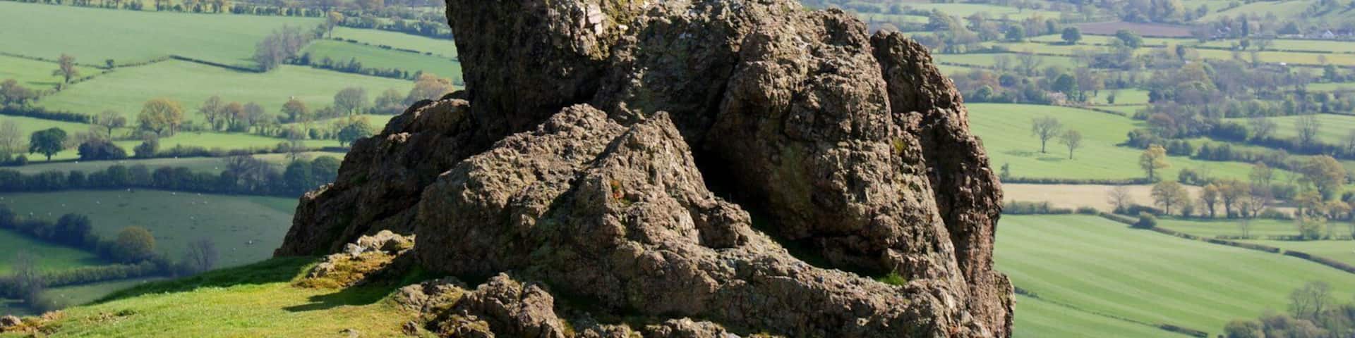 A rocky outcrop in a green field with rolling hills in the background.