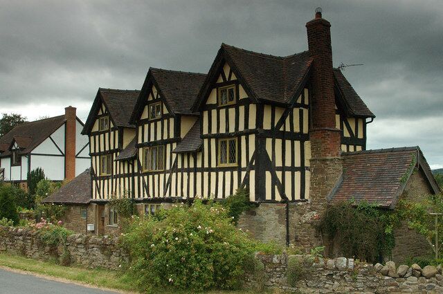 A Tudor-style building with black and white timber framing, a stone wall, and a stone pathway.
