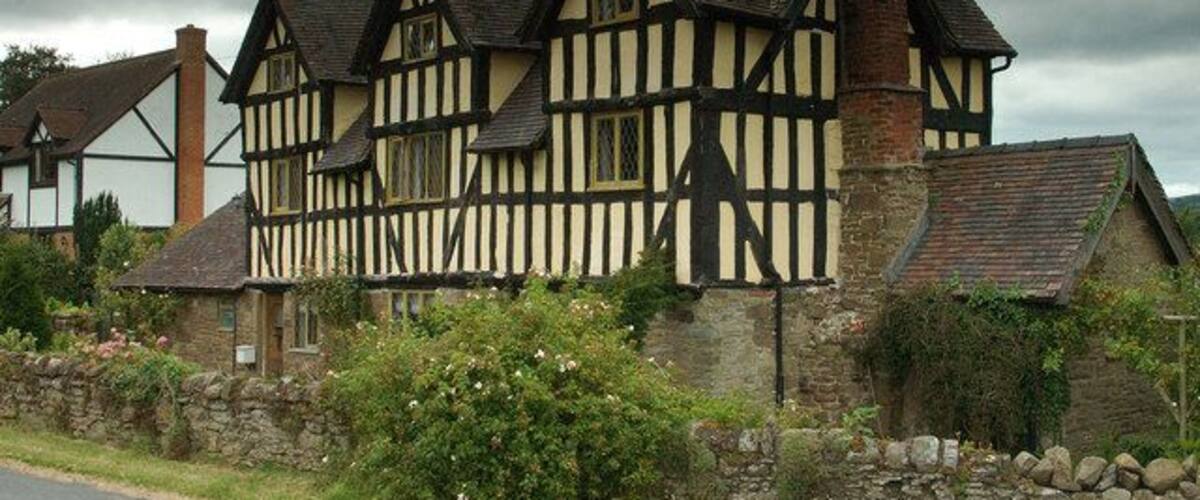 A Tudor-style building with black and white timber framing, a stone wall, and a stone pathway.