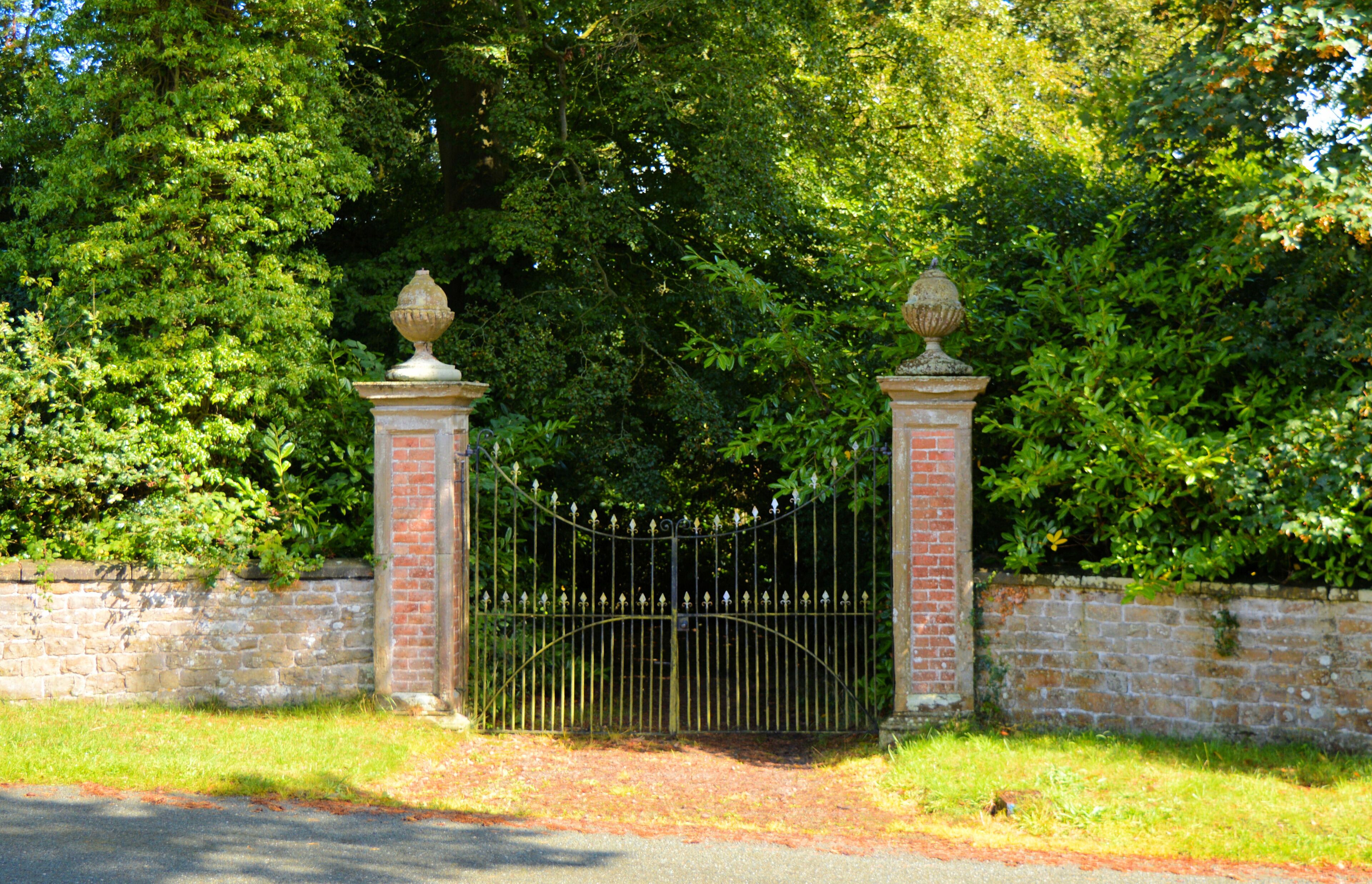 A gated entrance with a brick wall and metal gate, surrounded by lush greenery.