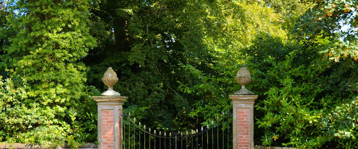 A gated entrance with a brick wall and metal gate, surrounded by lush greenery.