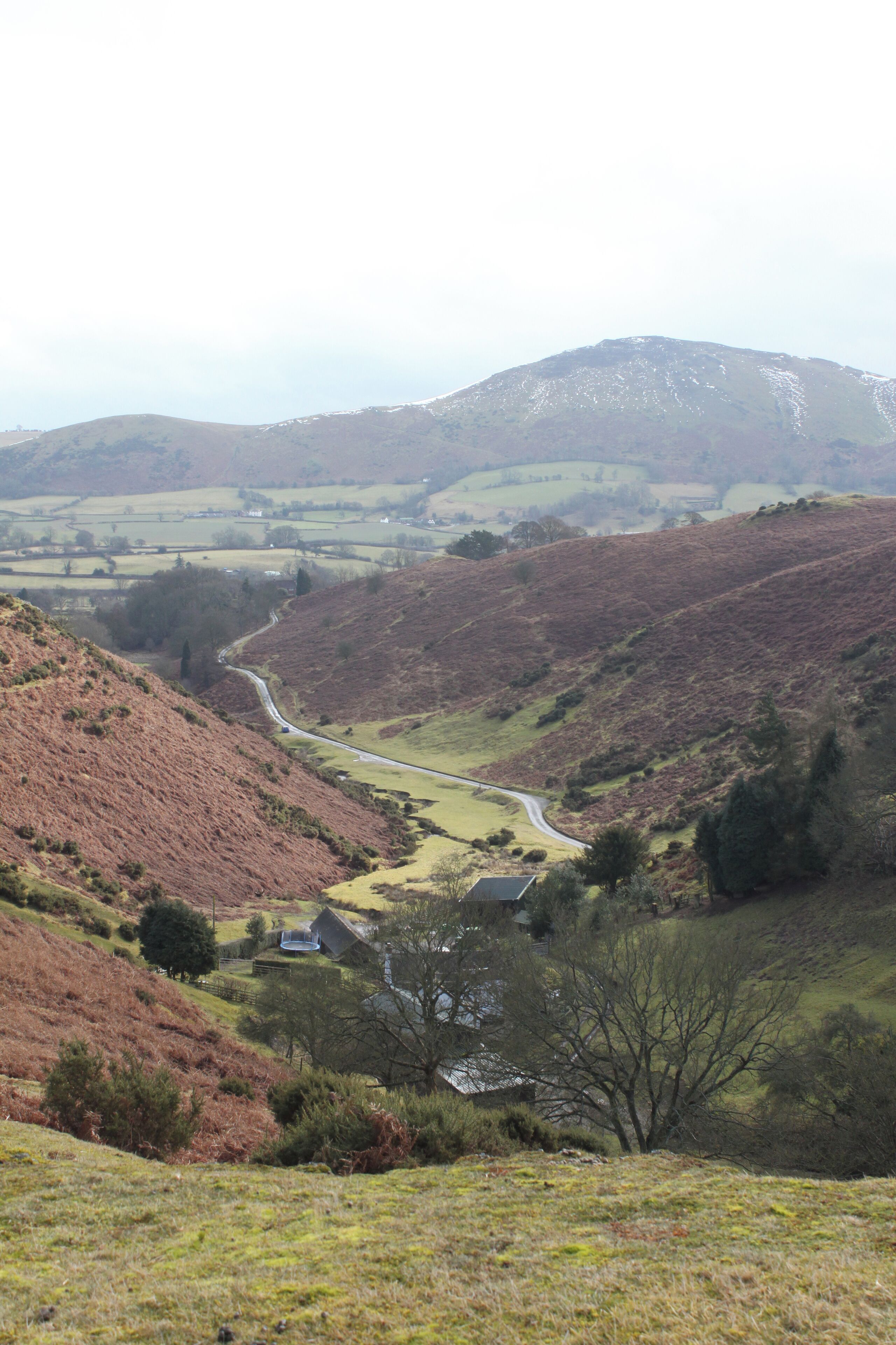 A winding road through a hilly landscape with sparse vegetation and a few buildings.