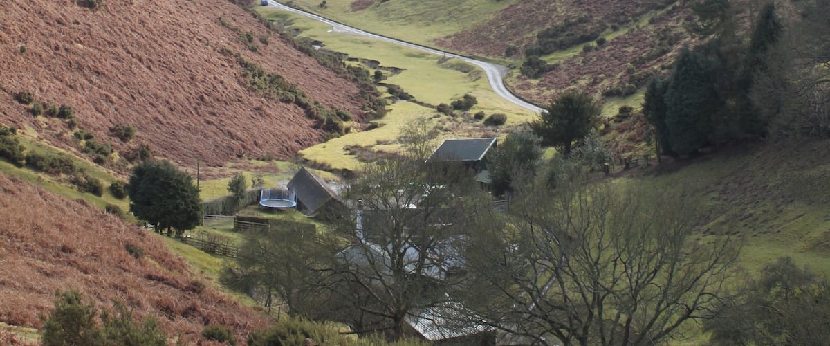 A winding road through a hilly landscape with sparse vegetation and a few buildings.