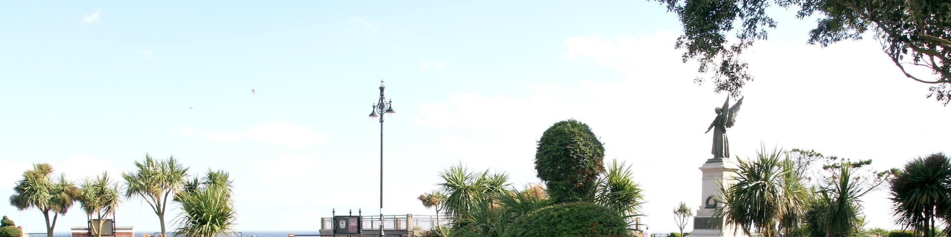 A landscaped garden with vibrant flower beds, a central topiary, and a statue.