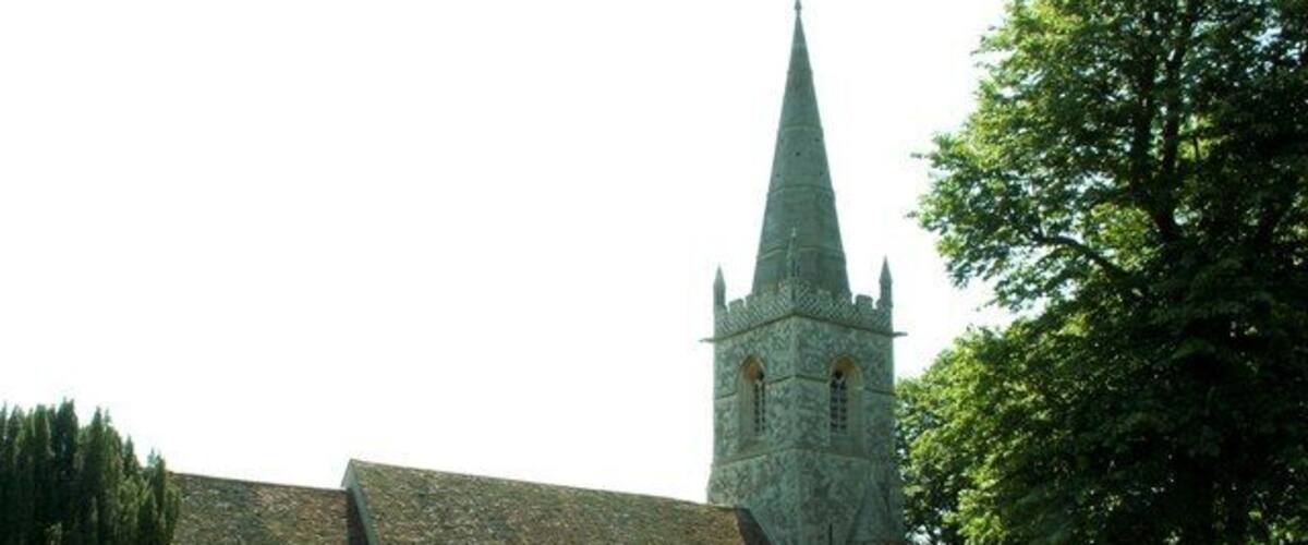 A church with a tall spire and a stone wall in front.