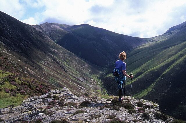 A person hiking on a rocky mountain path with a valley in the background.