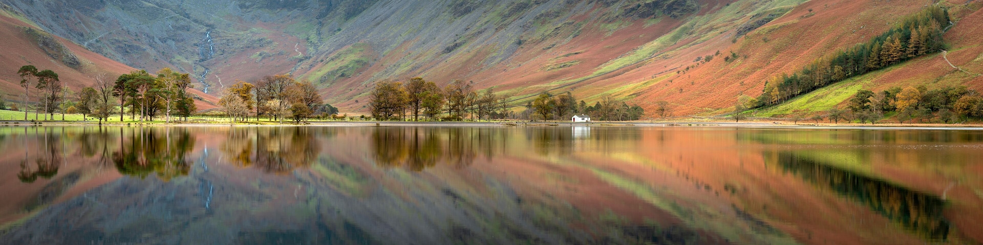 A tranquil lake with a mountain backdrop, surrounded by trees and a small white building.