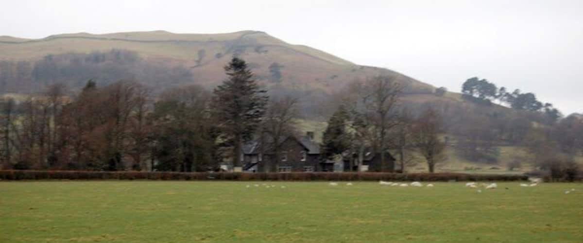 A rural landscape with a hill, a field, and a cluster of houses.