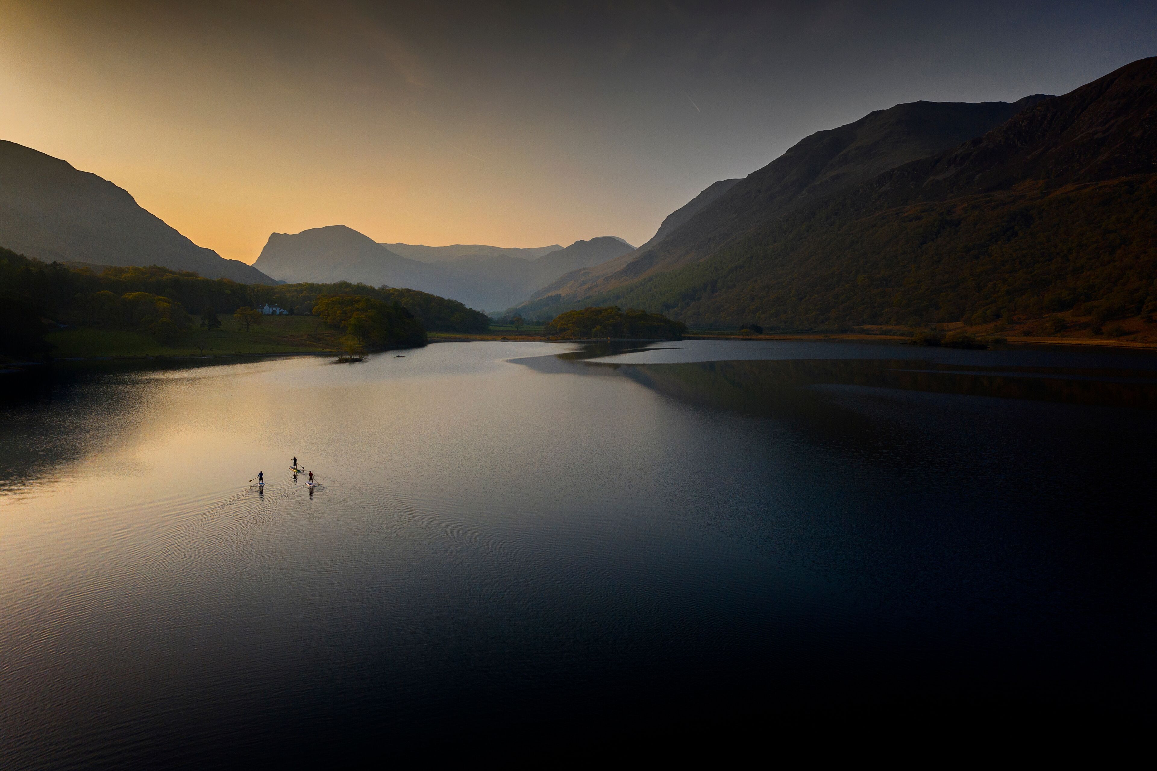Early morning paddle boarders sail across Crummock Water a lake in the Lake District part of the UNESCO World Heritgae Centre in Cumbria.
