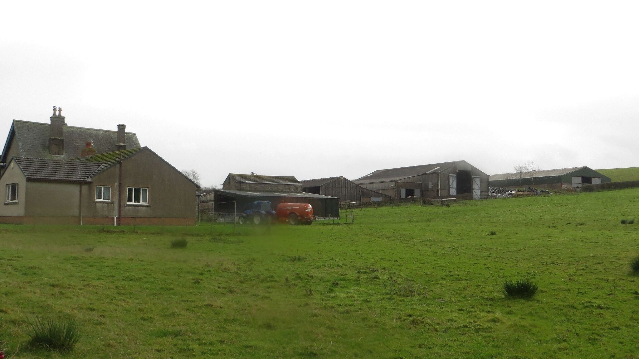 A rural landscape with a large green field, a farmhouse, and several barns.