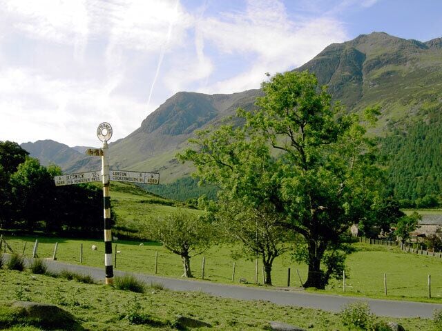 A signpost in a rural landscape with a mountain in the background.