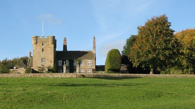 A historic stone building with a tower, surrounded by a well-maintained lawn and a large tree.
