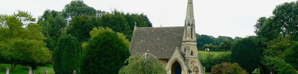 Eine Kirche mit einem hohen Kirchturm, umgeben von einem Friedhof mit Grabsteinen und üppigem Grün.