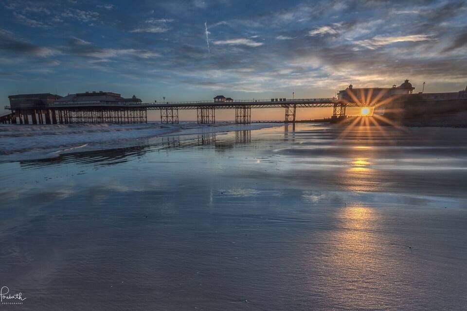 A pier extending into calm waters at sunset with a clear sky.