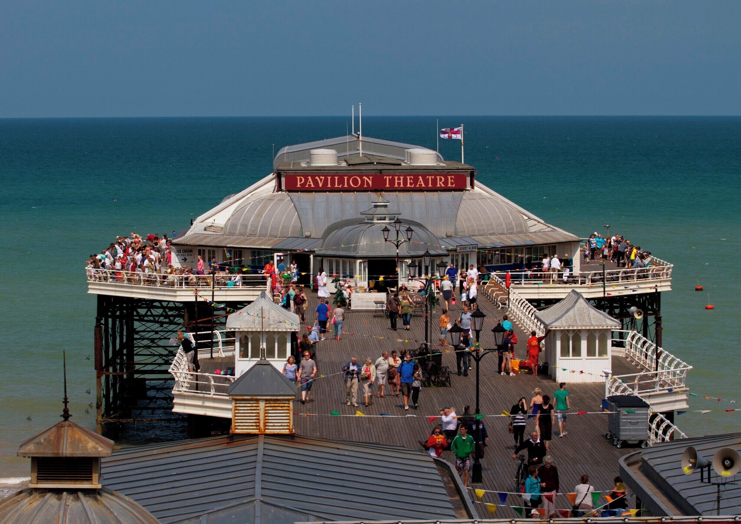 A pier with a Pavilion Theatre, surrounded by people and the sea.