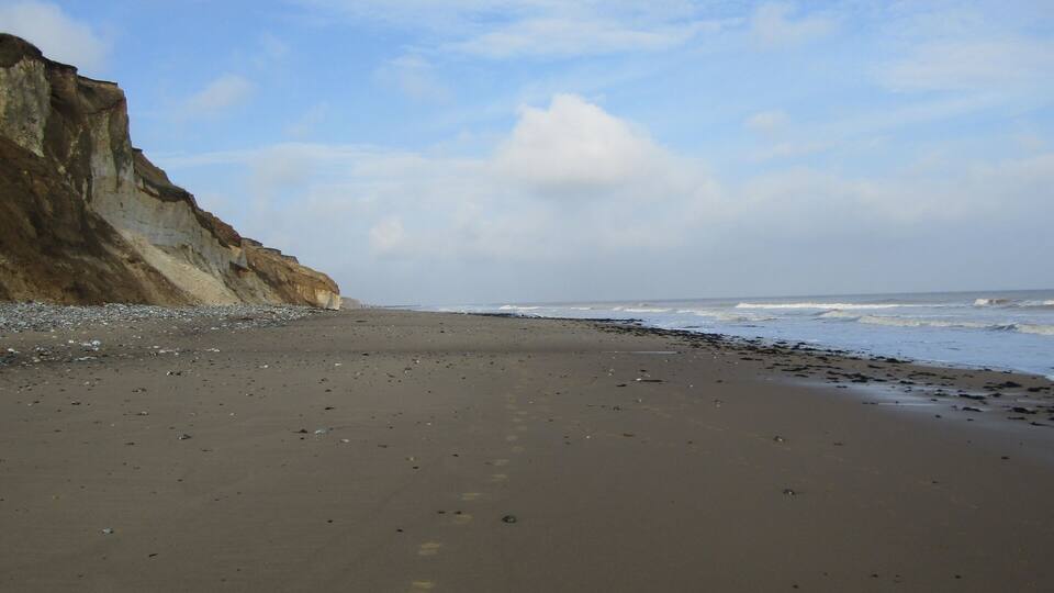 A beach with a rocky cliff and waves crashing onto the shore.