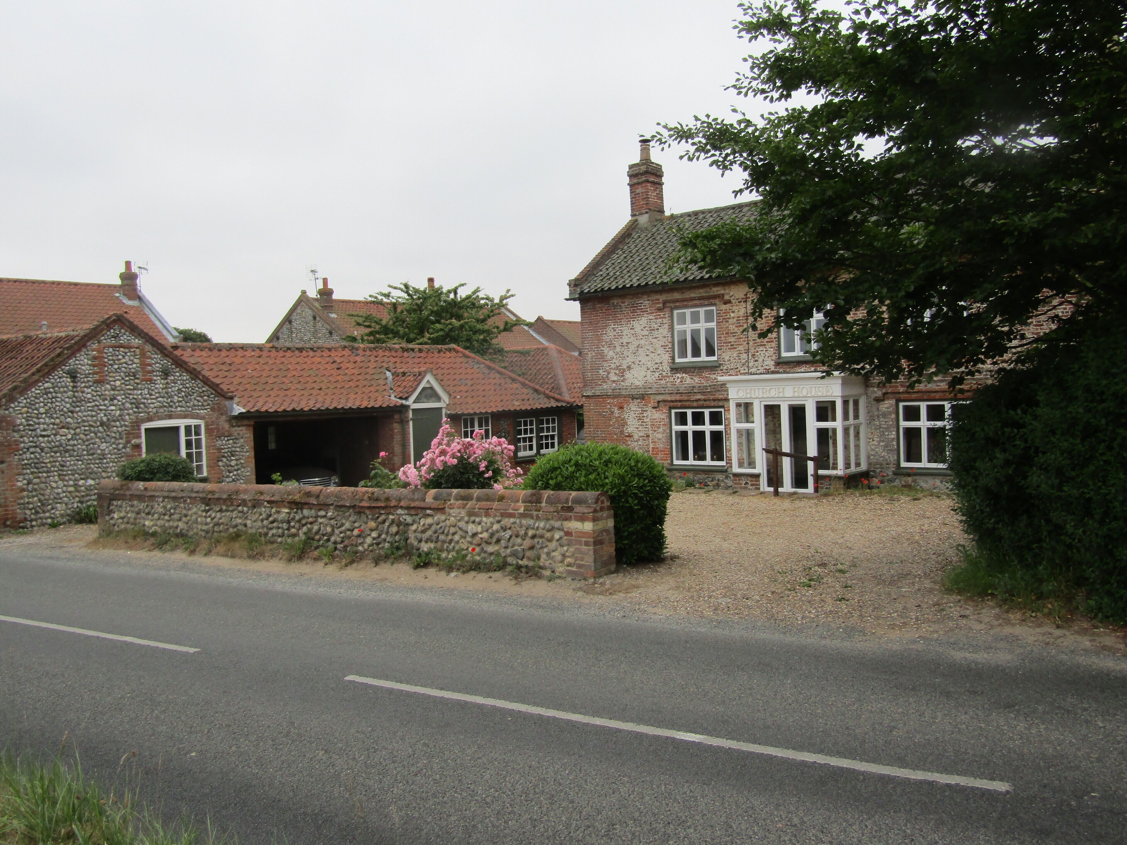 A stone church house with a gravel driveway and pink flowers in the foreground.