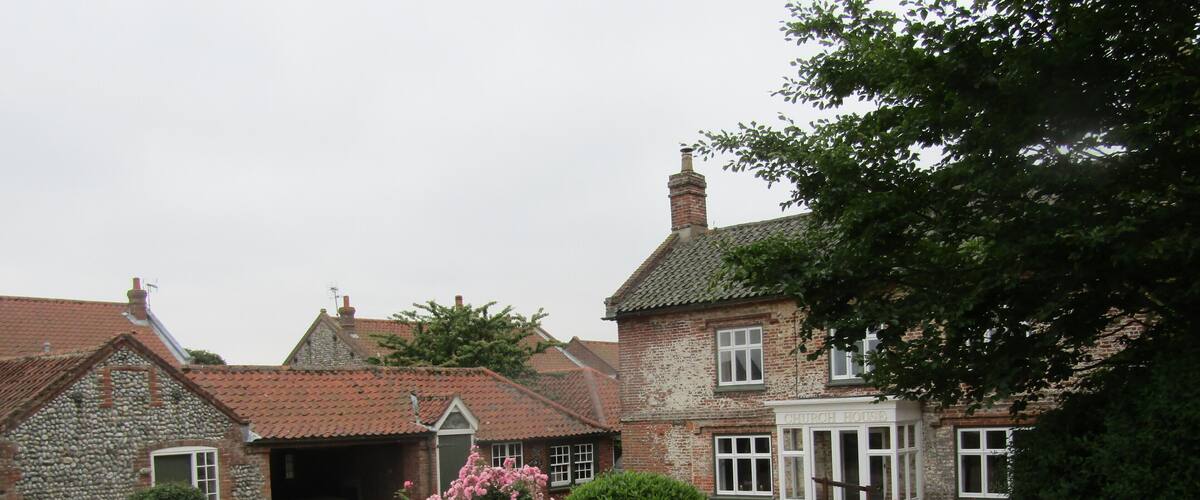 A stone church house with a gravel driveway and pink flowers in the foreground.