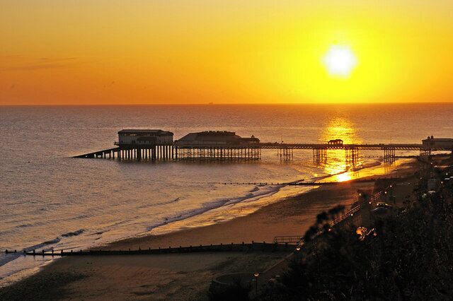 A sunset over a beach with a pier extending into the water.