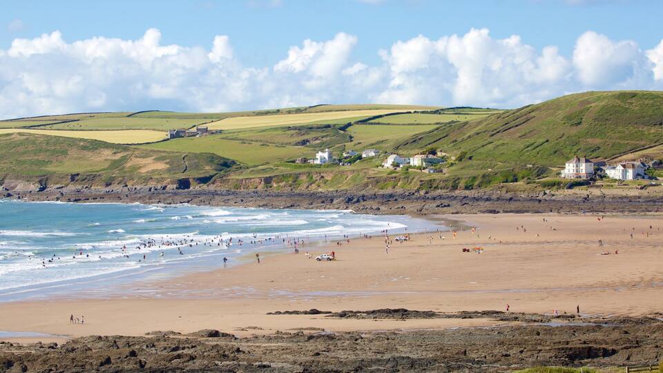 A coastal beach with waves, a sandy shore, and houses on the hillside.