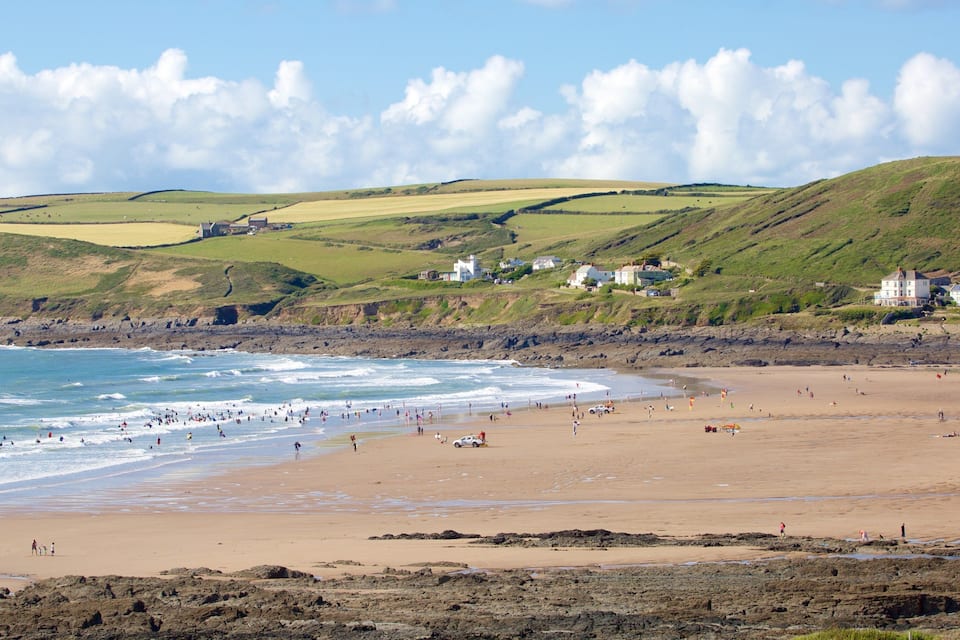 A coastal beach with waves, a sandy shore, and houses on the hillside.