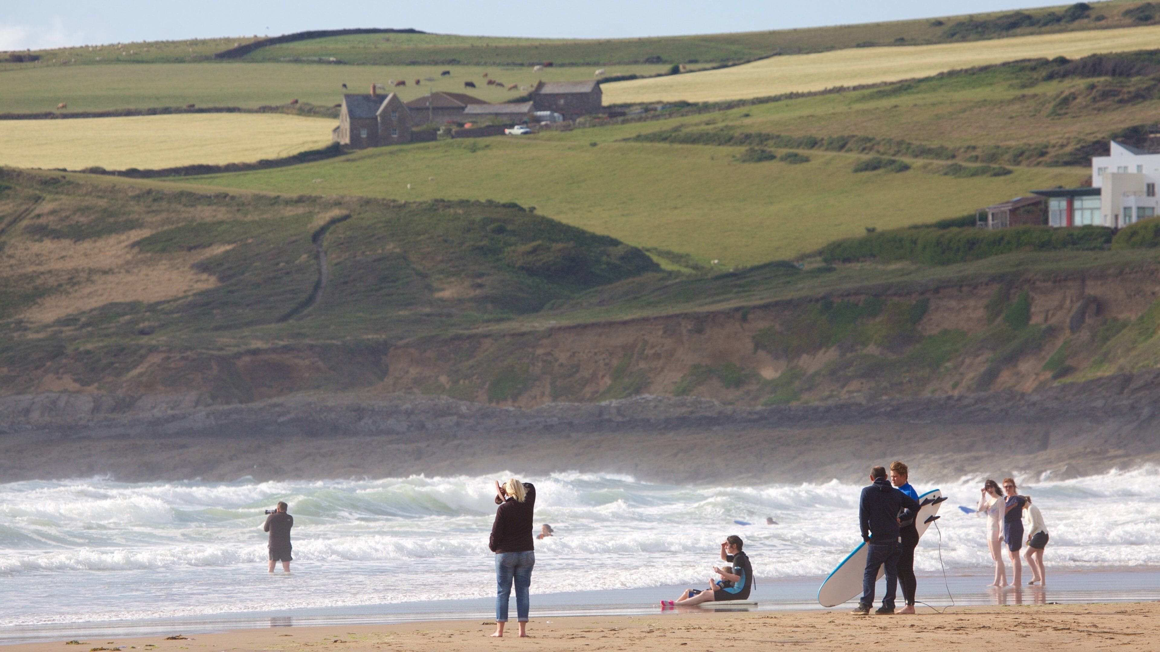 A coastal landscape with rolling hills, a beach, and a few buildings in the distance.