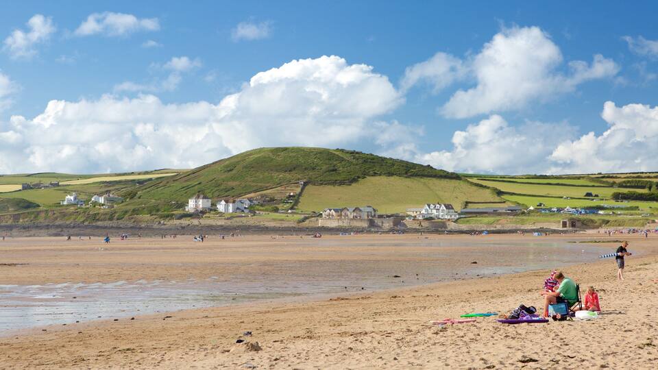 A sandy beach with houses and a hill in the background.