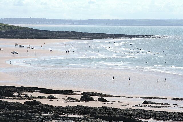 A beach with people walking and vehicles parked along the shore.