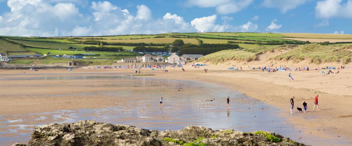 Une plage animée, un premier plan rocheux et, au loin, des collines verdoyantes.