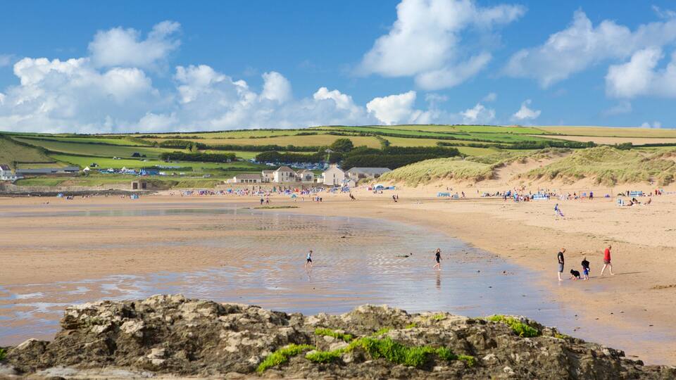 A beach with people, a rocky foreground, and green hills in the background.
