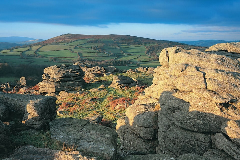 A rocky landscape with a view of rolling hills and distant mountains under a clear sky.